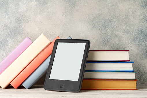 Digital tablet with a stack of books on gray background close up