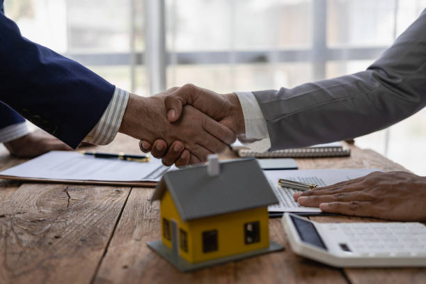 a sales representative shakes hands with a customer and offers a home purchase contract to purchase the current home and a proposed lease for the homeowner. close-up. - house real estate key residential structure imagens e fotografias de stock