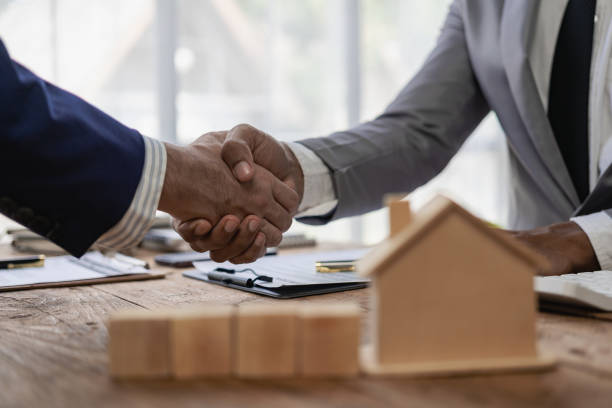 A sales representative shakes hands with a customer and offers a home purchase contract to purchase the current home and a proposed lease for the homeowner. Close-up.