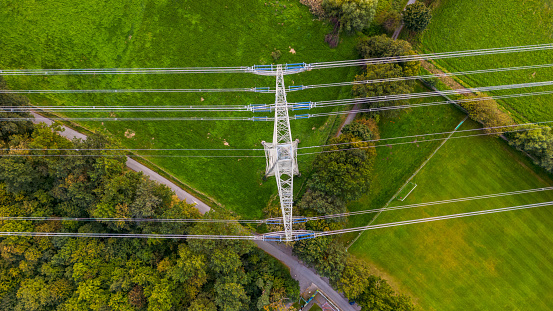 A man made steel tower with power lines in the middle of nature, trees and meadows in Germany