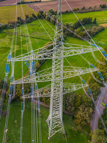 Drone shot of high voltage pylon with many power lines in green nature as conflict of technology and civilization