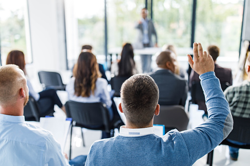 Back view of a businessman raising his hand to ask a question on education event in board room.