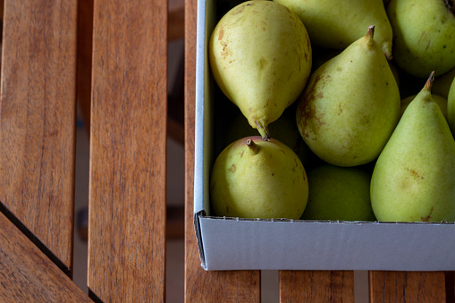 Pears in a cardboard box on a wooden table in overhead view