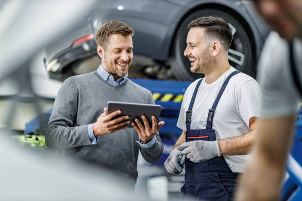 feliz cliente y mecánico de automóviles usando touchpad en un taller. - auto repair shop mechanic digital tablet customer fotografías e imágenes de stock