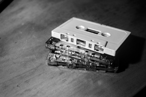 Monochrome old audio cassettes stacked on a wooden table.