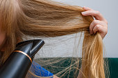 A woman dries her long blonde hair with an electric dryer