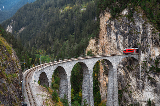 view from above on Landwasserviadukt railroad bridge in Switzerland with red train entering tunnel