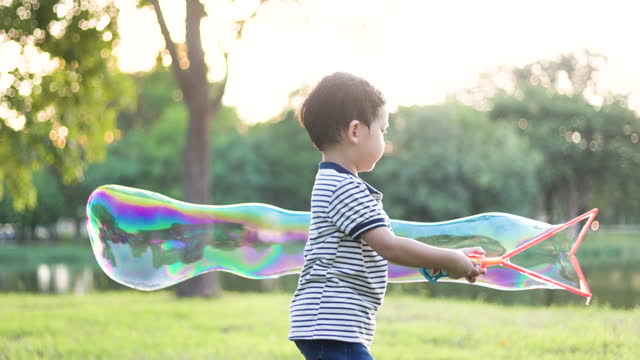 Little Asian boy playing soap bubble on the yard public park
