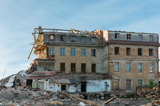 A large destroyed building with broken apartments and a pile of construction debris. House damaged by terrorist attack, war or earthquake background.