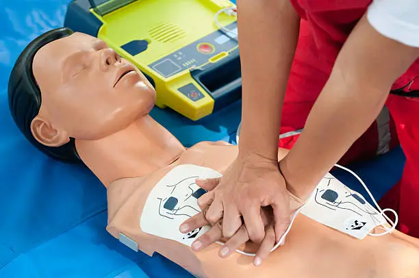 CPR training - Chest compressions combined with defibrillator operation performed on a CPR dummy. Focus on hands