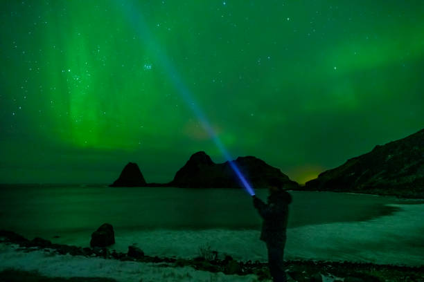 istock Man with a flashlight looking at Northern Lights, Aurora Borealis over the Lofoten 1742260669