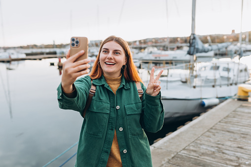 Happy Women taking selfie. Young beautiful girl say Hi, Tourist walking along the waterfront, seaside. Vacation concept by exploring interesting places to travel