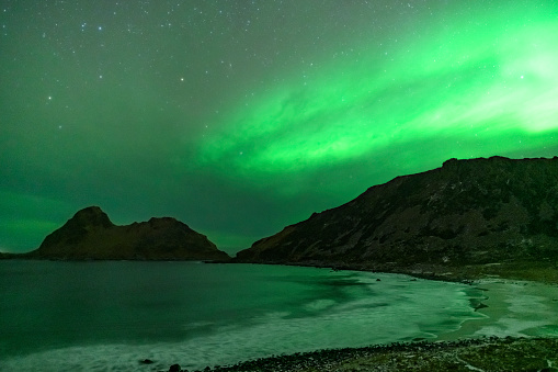 Norhtern Lights or aurora  over Nykvag beach with a starry sky in Northern Norway during a cold winter night.