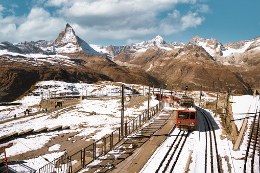 low angle view on red train coming down mountain in the swiss alps with matterhorn in the background