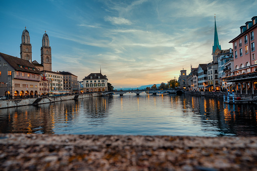 view from the bridge on illuminated cityscape of old town zurich at riverside at sunset hour