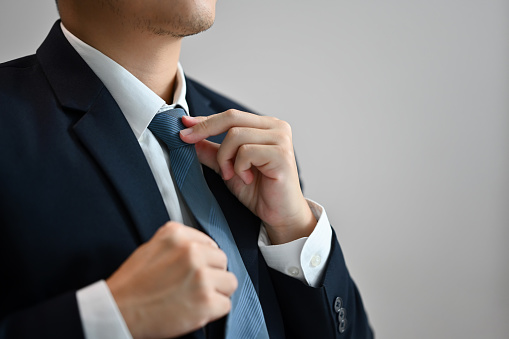Close up of a businessman in formal clothes adjusting his necktie on white background.