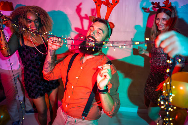 Group of cheerful young friends having fun doing limbo dance passing under Christmas lights at New Year Eve party