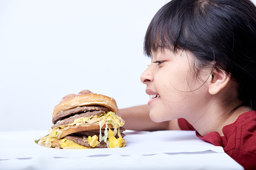 Cute little girl eating an appetizing cheeseburger on white background