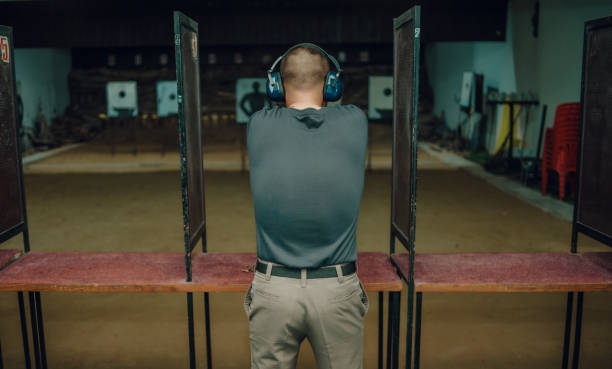 A professional man wearing earmuffs and goggles is practicing shooting a 9mm pistol inside a shooting range.