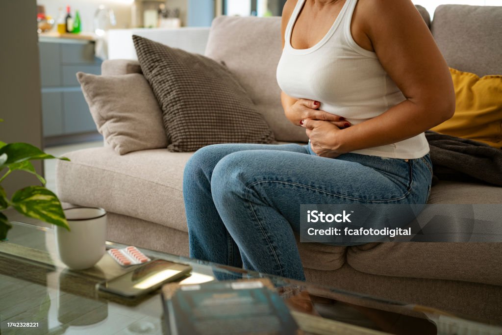 Woman sitting with hands on her abdomen suffering from stomach cramps Irritable Bowel Syndrome Stock Photo