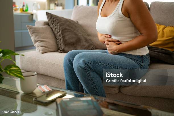 Woman Sitting With Hands On Her Abdomen Suffering From Stomach Cramps Stock Photo - Download Image Now