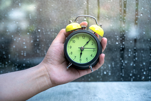 Human hand holding alarm clock with a clear window and raindrop background