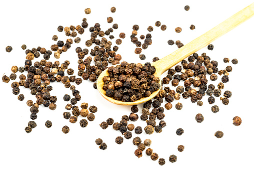 Black peppercorns with wooden spoon over white table in the kitchen at home.