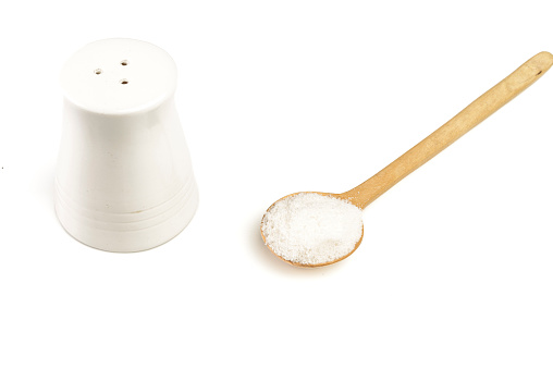 Close up view of wooden spoon with seasoning salt and shaker on white table in the kitchen at home