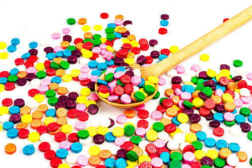 Sugar sprinkles on wooden spoon over white table in the kitchen at home.