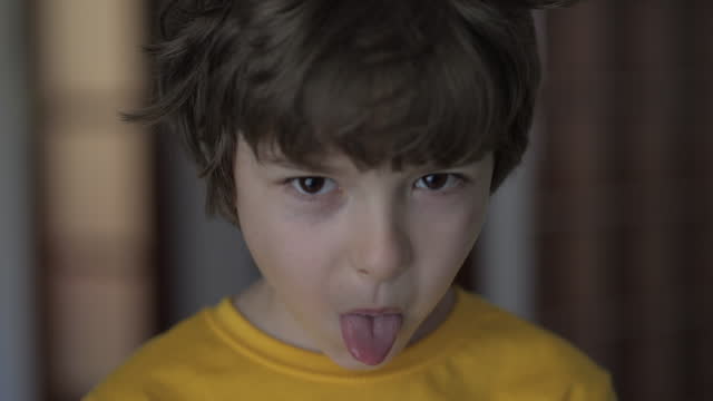 Angry Boy Shows Her Tongue in Funny Grimace. Little Boy Grimacing And Sticking Out Tongue. Close-up Portrait of Emotional Child Sticking Out His Tongue And Showing Grimaces. Kid Sticking Out Tongue.