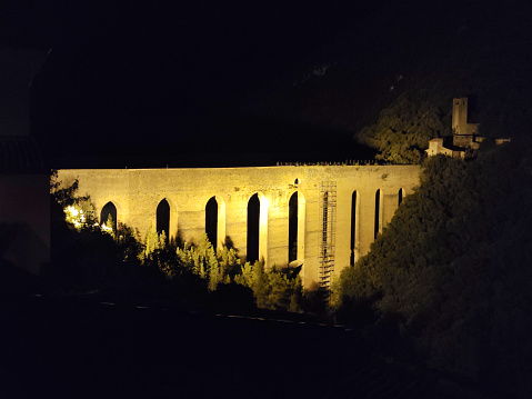 The ancient ponte delle Torri arch bridge by night in Spoleto, Umbria. At the two ends of the bridge there are two fortresses, the Rocca Albornoziana and the Fortilizio dei Mulini, built to guard the bridge and active as a mill until the 19th century.