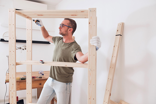 Man assembling new wooden shelf and furniture in the apartment.