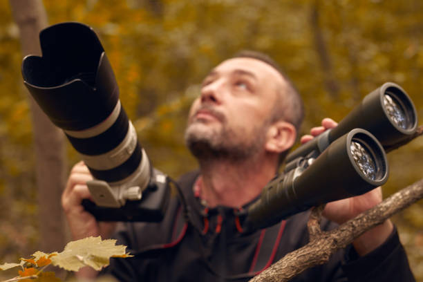 Man using binoculars and camera for birdwatching and other observing animals in nature.
