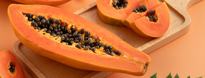Fresh cut papaya fruit over orange table background for tropical gourmet design concept.