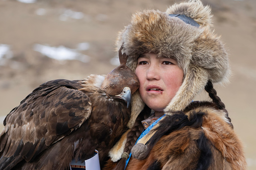 Bayan-Olgii Province, Mongolia - October 1, 2023: A golden eagle rests its head on teenager Aimuldir D., an ethnic Kazakh female eagle hunter and eventual winner of the Ulgii Golden Eagle Festival.