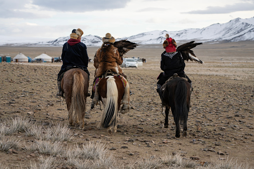 Bayan-Olgii Province, Mongolia - October 1, 2023: Teenager Aimuldir D. (middle), an ethnic Kazakh female eagle hunter and eventual winner of the Ulgii Golden Eagle Festival, rides horseback with family members at the end of the festival.
