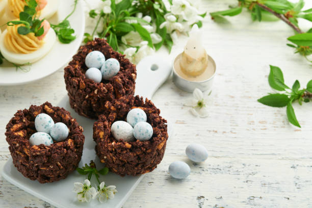 istock Easter brunch or breakfast. Easter chocolate nest cake with chocolate candy eggs, traditional hot cross buns and deviled eggs with bouquets of blooming apple trees. Spring Easter holiday food concept. 1742374529