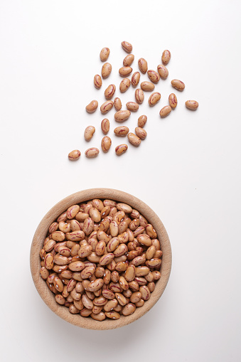 borlotti beans inside a wooden bowl on a white background with a top view