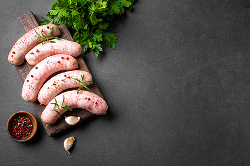 Raw sausages with spices and rosemary on cutting board, black background, copy space. Cooking ingredients. Natural healthy food concept, top view.