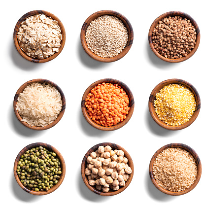 Various grains in wooden bowls isolated on white background, top view. Set of uncooked grains and legumes.