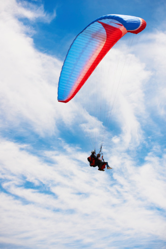 A paraglider takes off from a mountainside with a blue and white canopy and the sun behind. A paraglider is a silhouette. The glider is sharp, with little wing movement. A male paraglider launches a paraglider into the air.