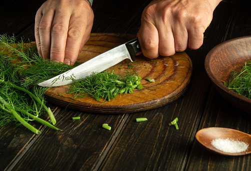 Slicing fennel or dill with a knife in the hands of a chef on a kitchen cutting board before preparing national or vegetarian dishes. Provisioning or canning fennel.