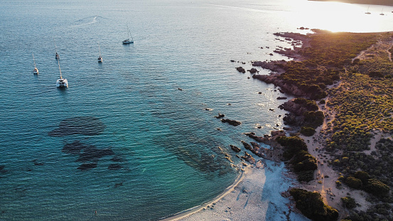 Aerial shot of a heavenly Corsican creek at sunset, with sailboatsat anchor, rocks, bushes and turquoise water.