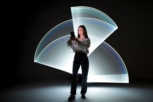 Young woman using a smart phone in front of a light shape.