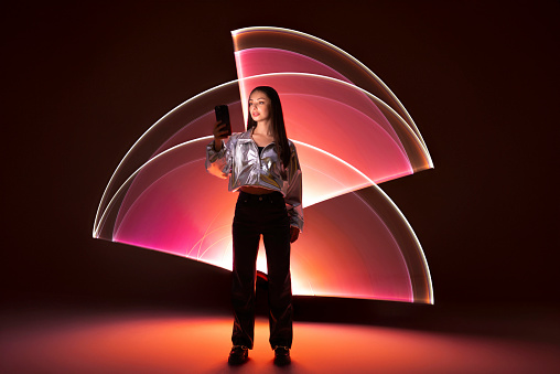 Young woman using a smart phone in front of a light shape.