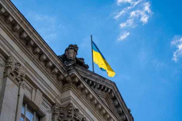 A government building in Berlin with a flag of Ukraine on the roof and fluttering in the wind against a blue sky with few veil clouds