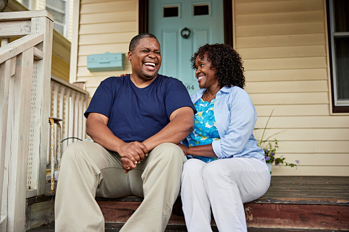 Front view of casually dressed man and woman in mid 40s and early 50s sitting on top step, side by side, relaxed and comfortable with each other.