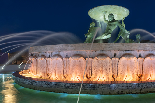 The Tritons’ Fountain is a fountain located just outside the City Gate of Valletta, Malta. It consists of three bronze Tritons holding up a large basin, balanced on a concentric base built out of concrete and clad in travertine slabs. The fountain is one of Malta's most important Modernist landmarks, designed and constructed between 1952 and 1959.\n\nValletta is an administrative unit and the capital of Malta which is an island country in Southern Europe, located in the Mediterranean Sea.