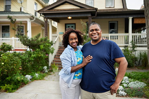 Cheerful Black couple in front of restored Victorian home