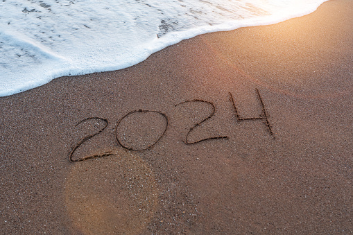 New Year 2024 is written by hand on the surface of the sand on the seashore or ocean. Freedom to relax and travel in the new year